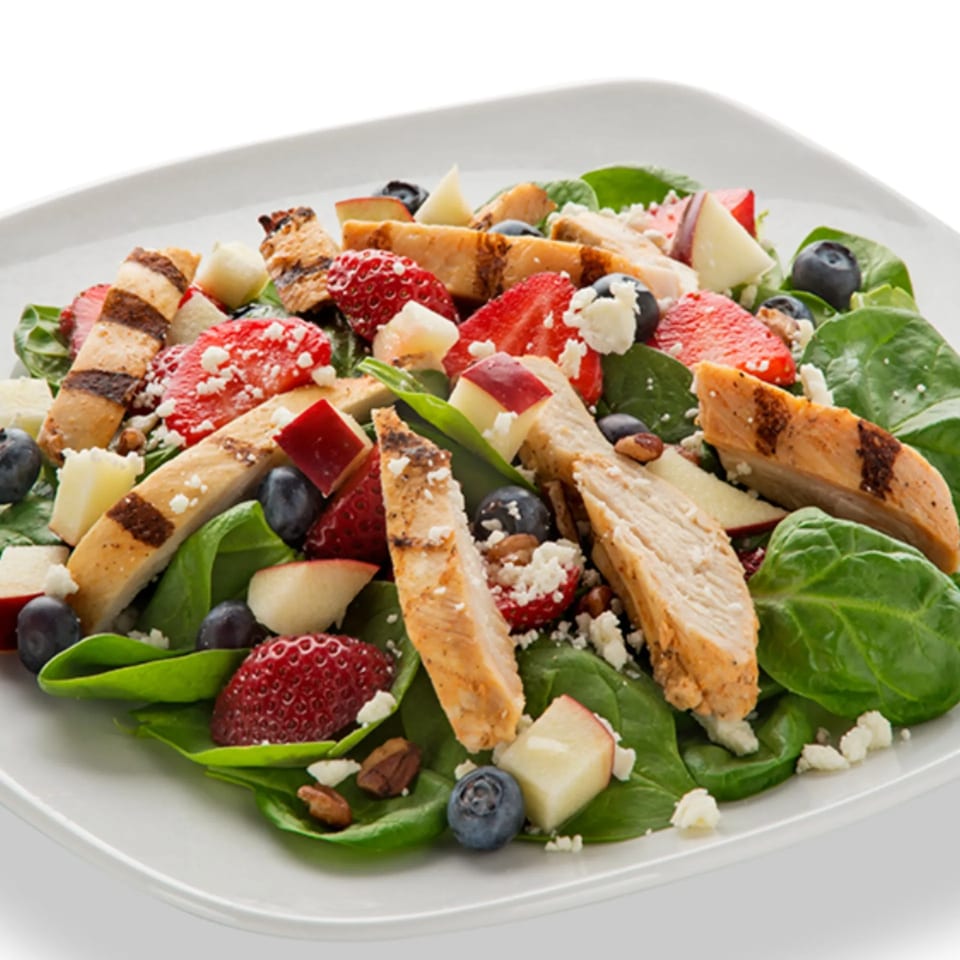 Grilled chicken salad with spinach, strawberries, blueberries, apples, and feta cheese.